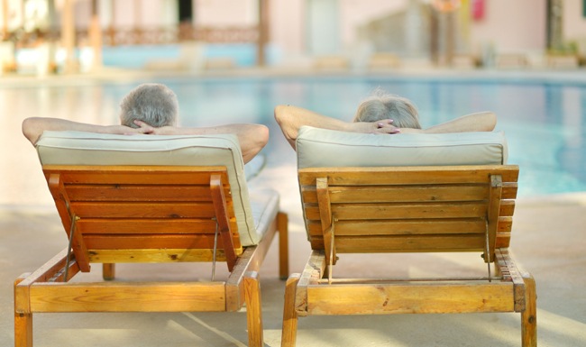 lifestyle image of a couple sitting on lounging chairs beside a pool