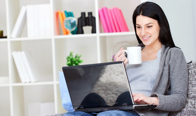 lifestyle image of a woman on her laptop while holding a mug